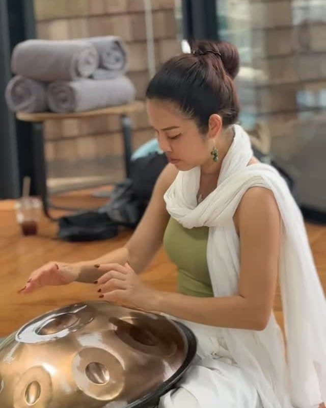 Kai playing the handpan in the teak-floored shala, rolled mats behind her